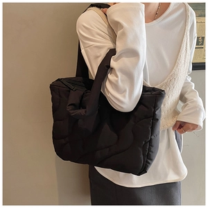 Detail of a black quilted puffer tote bag shown on model for realistic size and style guide