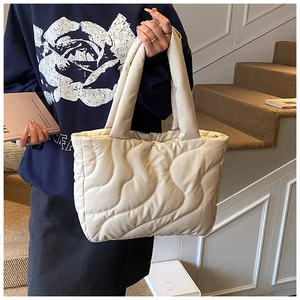 Detail of beige quilted puffer tote bag showing wavy stitching and soft padded texture