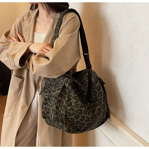 Detail of a large camouflage canvas tote bag with a side pocket worn by a model