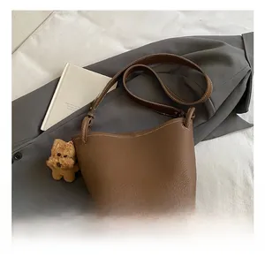 Detail of dark brown lychee leather bucket bag with white stitching and plush dog charm