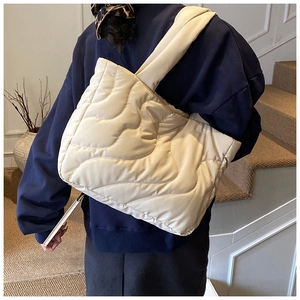Detail of a large cream-colored quilted tote bag with soft wavy texture and wide strap