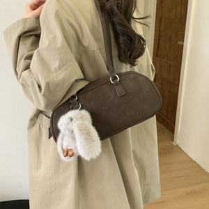 Detail of dark brown retro Boston bag with plush bunny charm on khaki trench coat