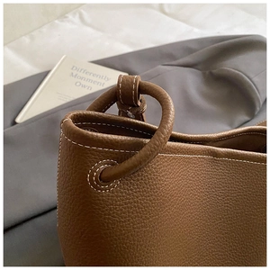 Close-up of brown litchi grain leather texture and white contrast stitching on the bag