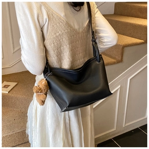 Detail of black lychee grain bucket bag with white stitching and bear charm on model