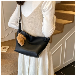 Detail of black pebbled leather bucket bag with white contrast stitching and bear charm