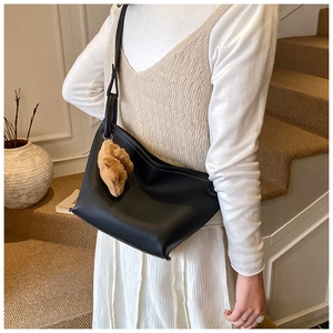 Detail of black pebbled leather bucket bag with white stitching and cute bear charm