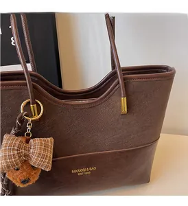 Detail of vintage brown tote bag with litchi grain texture and bear head charm
