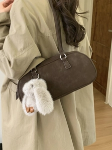 Brown vintage Boston shoulder bag with plush rabbit charm over a beige trench coat