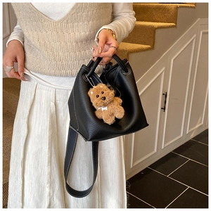 Detail of black pebbled leather bucket bag with white contrast stitching and bear charm
