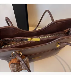 Detail of dark brown leather tote bag with gold zipper and plaid bear charm accessory