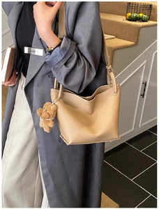 Close-up of beige lychee grain leather bucket bag with a cute brown plush bear charm