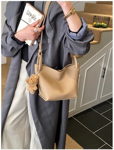 Detail of beige lychee leather bucket bag with a brown plush bear charm and adjustable strap