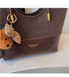 Detail of vintage brown tote bag with logo and cute plush bear charm accessory