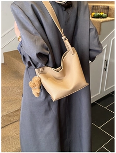 Beige pebble leather bucket bag shown on a shoulder with a cute brown plush bear charm