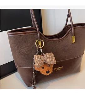 Detail of dark brown tote bag with plush teddy bear charm and gold logo lettering