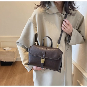 Detail of vintage dark brown leather crossbody bag with metal buckle on beige trench coat