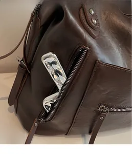 Macro shot of dark brown leather tote showing zipper pocket storage and rivet detail