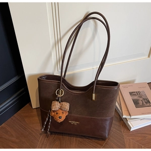 Detail of dark brown tote bag featuring leather stitching and a cute teddy bear charm