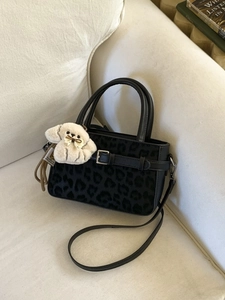 Elegante borsa leopardata nera con ciondolo in peluche su un morbido divano bianco