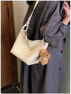 Close-up of off-white lychee texture tote bag featuring a cute brown teddy bear charm
