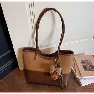 Detail of a brown patchwork tote bag with suede texture and a cute bear charm accessory