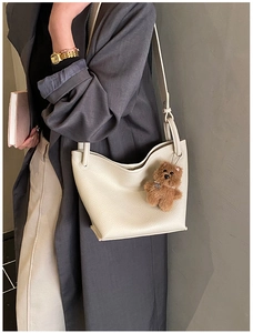 Detailed texture of white lychee leather bucket bag with a cute brown plush bear charm