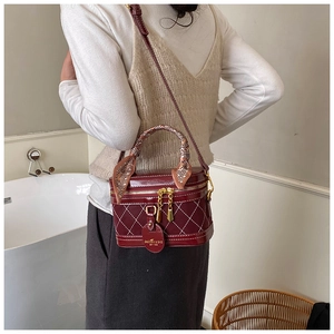 Vrouw met een bordeauxrode laks lederen box-tas met ruitpatroon en zijden sjaal handvat