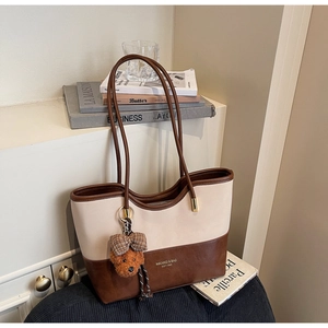 Close-up of contrast leather tote bag with brand logo and cute plush bear charm