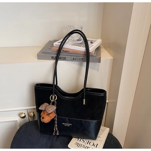 Detail of black tote bag featuring mixed textures, gold logo, and a plush charm accent