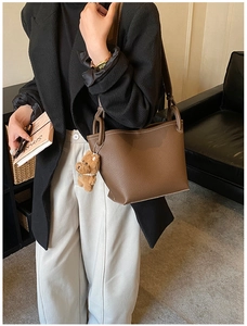 Detail of brown litchi leather tote bag with white stitching and plush bear charm