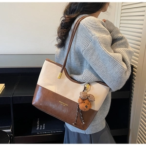 Detail view of contrast color tote bag with bear charm and metallic ring strap accents