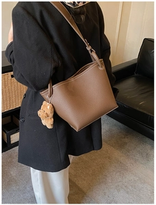 Close-up of brown pebbled leather bucket bag with white stitching and bear charm