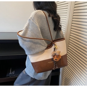 Detail view of two-tone tote bag in cream and brown with cute plush bear charm accessory
