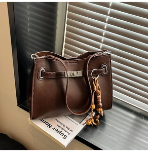 Detail of dark brown leather tote bag with silver buckle and bohemian wooden bead tassel