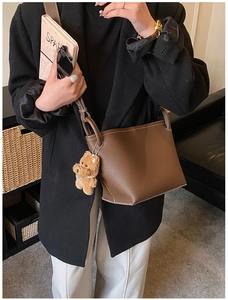 Detail view of dark brown leather crossbody bucket bag with teddy bear charm accessory