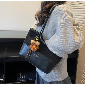 Detail of black leather tote bag with gold logo lettering and a plush puppy charm