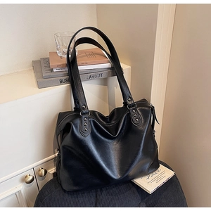 Close-up of black PU leather tote bag with silver rivets and wide shoulder straps