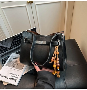 Detail of black faux leather tote bag with silver twist lock and retro beaded tassel charm