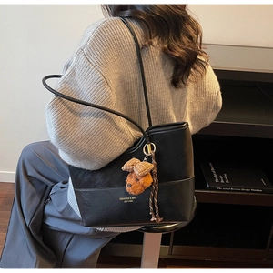 Detail of black glossy leather tote bag with gold lettering and plush bear charm