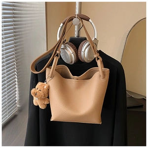 Detail of camel lychee leather bucket bag with cute plush teddy bear charm and strap