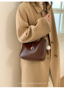 Detail of retro brown leather bucket bag with silver G buckle and white plush charm