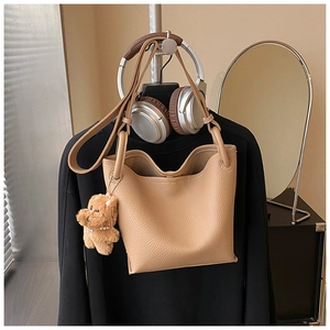 Close-up of a camel lychee leather bucket bag with a cute brown plush puppy charm