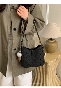 Detail of black polka dot shoulder bag with leather strap and white plush charm on model