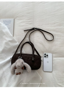 Detail of dark brown suede Boston bag with plush bunny charm on white fabric