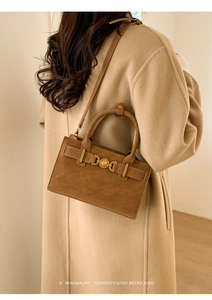 Detalle de bolso bandolera vintage marrón con hebilla de corazón dorada y abrigo beige