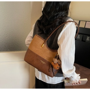 Detailed view of bicolor suede tote bag with plush bear charm and metallic buckle