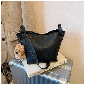 Detail of black lychee grain bucket bag with contrast stitching and plush dog charm