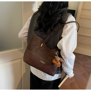 Detail of dark brown tote bag with contrast textures and cute teddy bear charm accessory