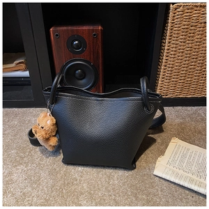 Close-up of black lychee grain leather bucket bag with contrast stitching and bear charm