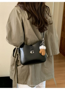 Detail of black matte leather shoulder bag featuring a metal G clasp and plush glove charm